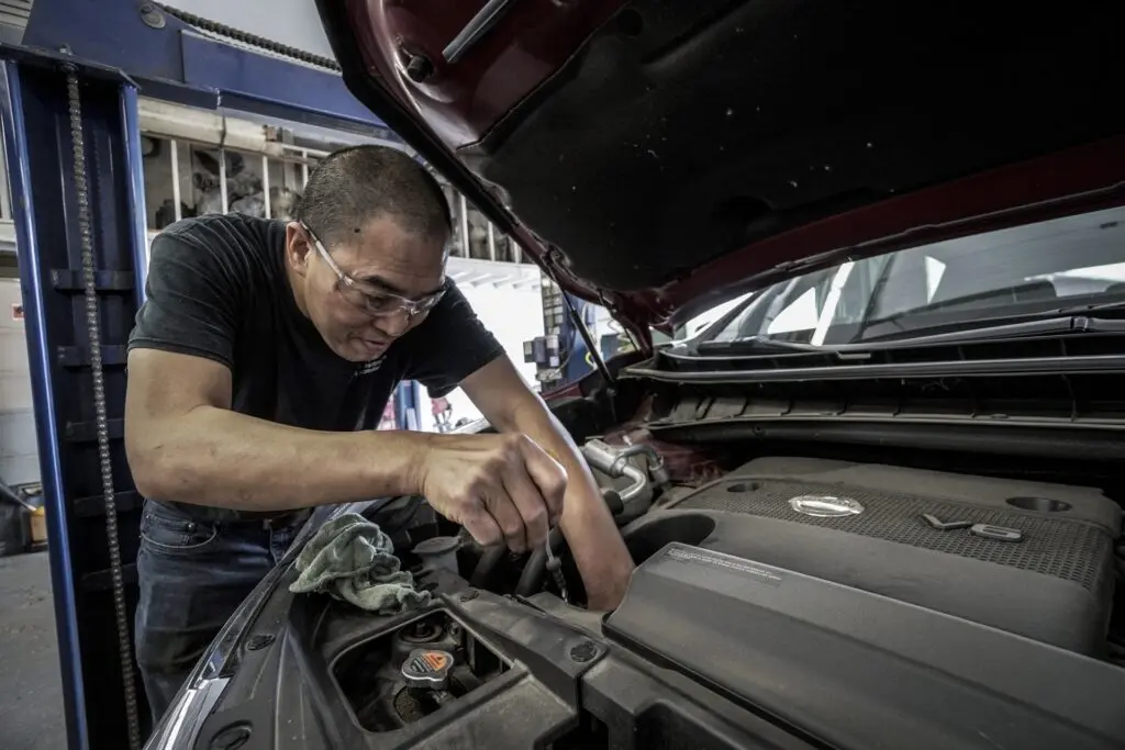 A man focused on repairing a car engine, tools in hand, surrounded by automotive parts in a workshop setting.