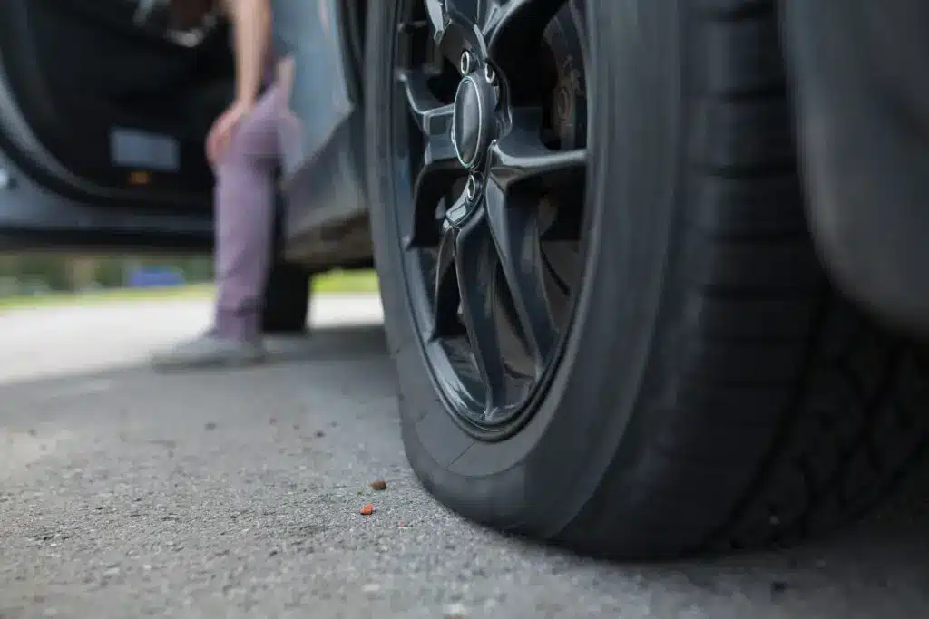 A person getting out of the car checking out the flat tire at the back