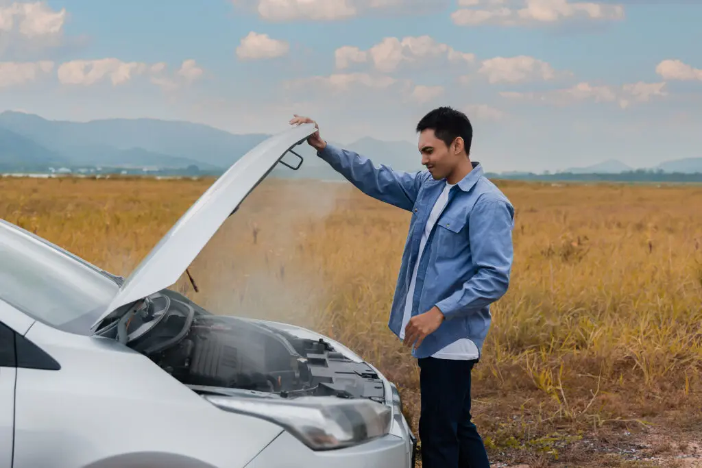 A man stands beside a broken car with the hood open, inspecting the engine for issues