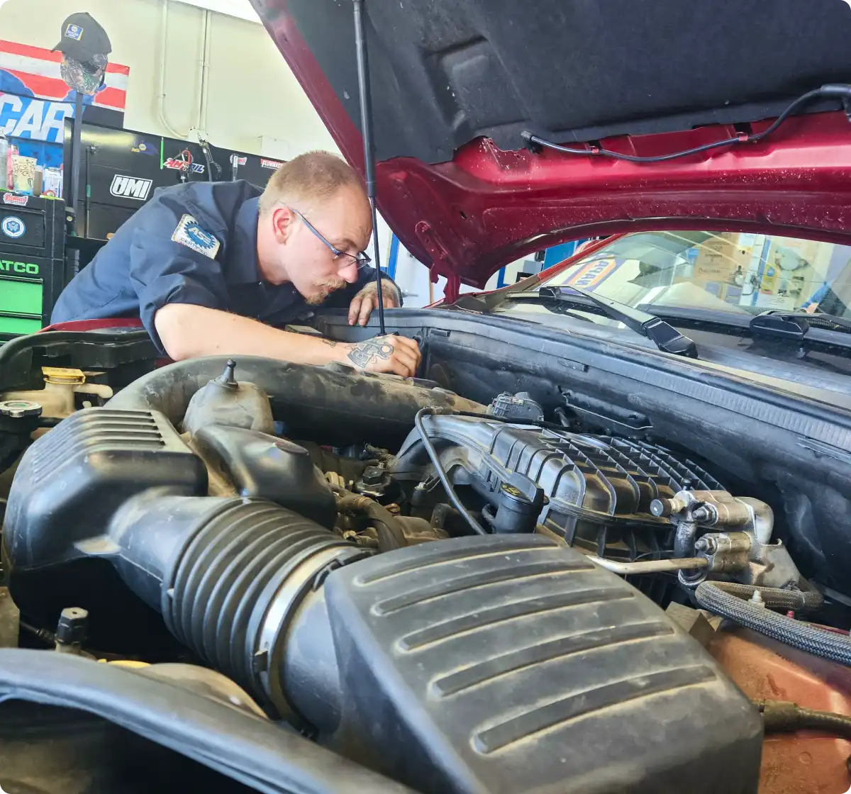 A mechanic hunched over and working on the hood of a red car