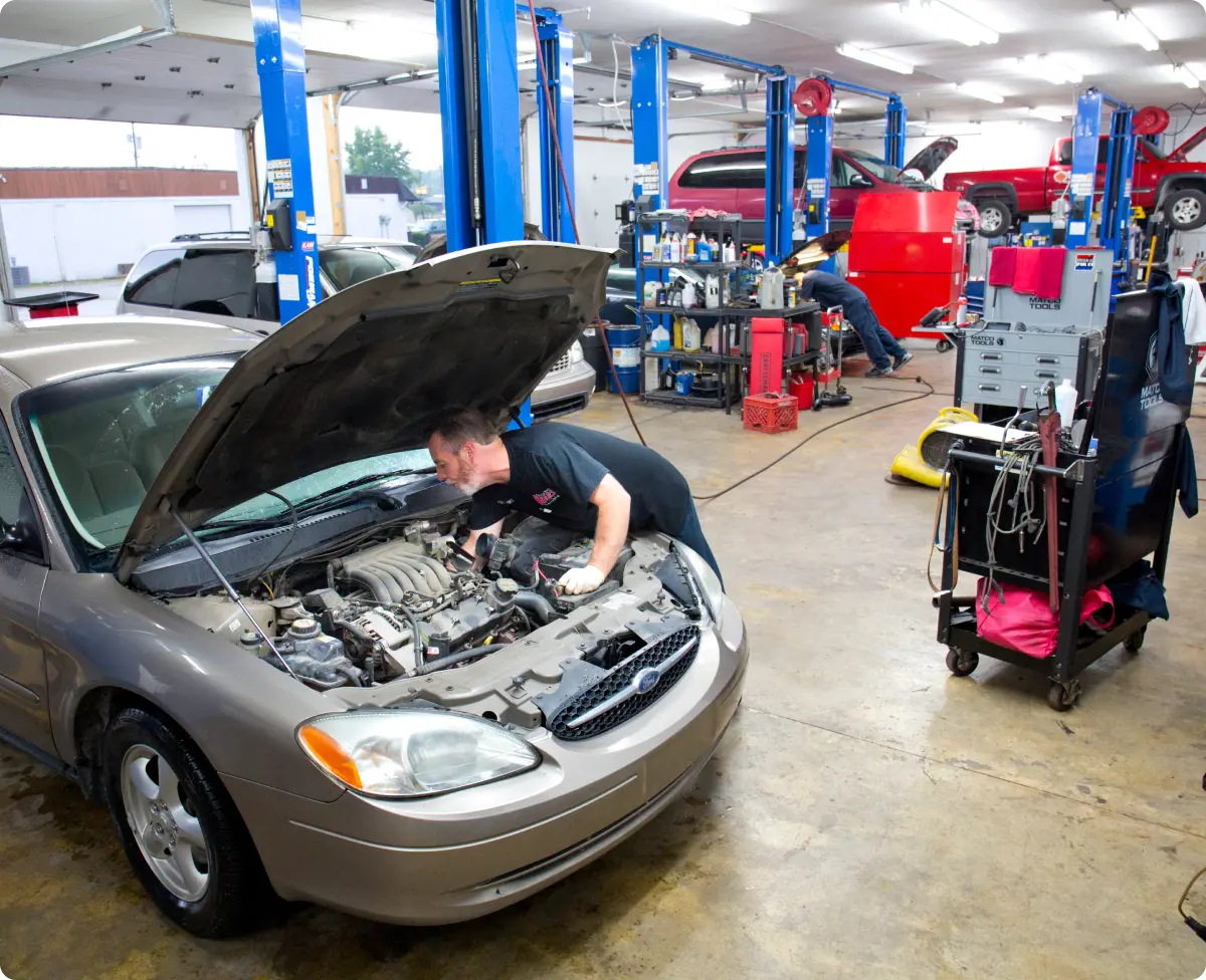 A man focused on repairing a car, tools in hand, demonstrating automotive skills in a garage setting.