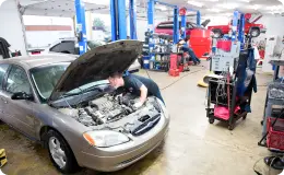 the interior of Express Repair Auto showing a mechanic working on the hood of a silver car