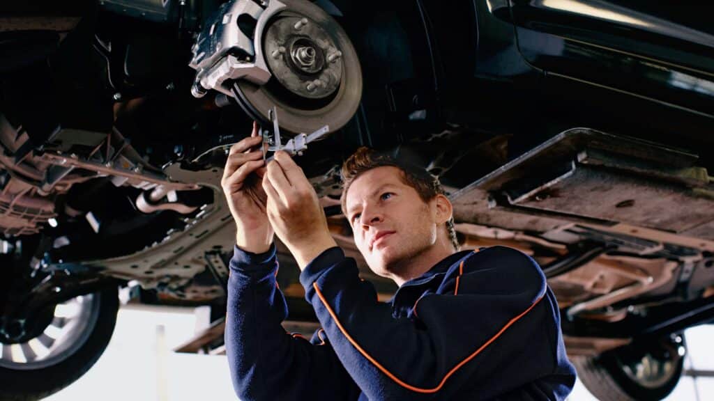 A man is repairing a car while positioned underneath the vehicle's suspension system.