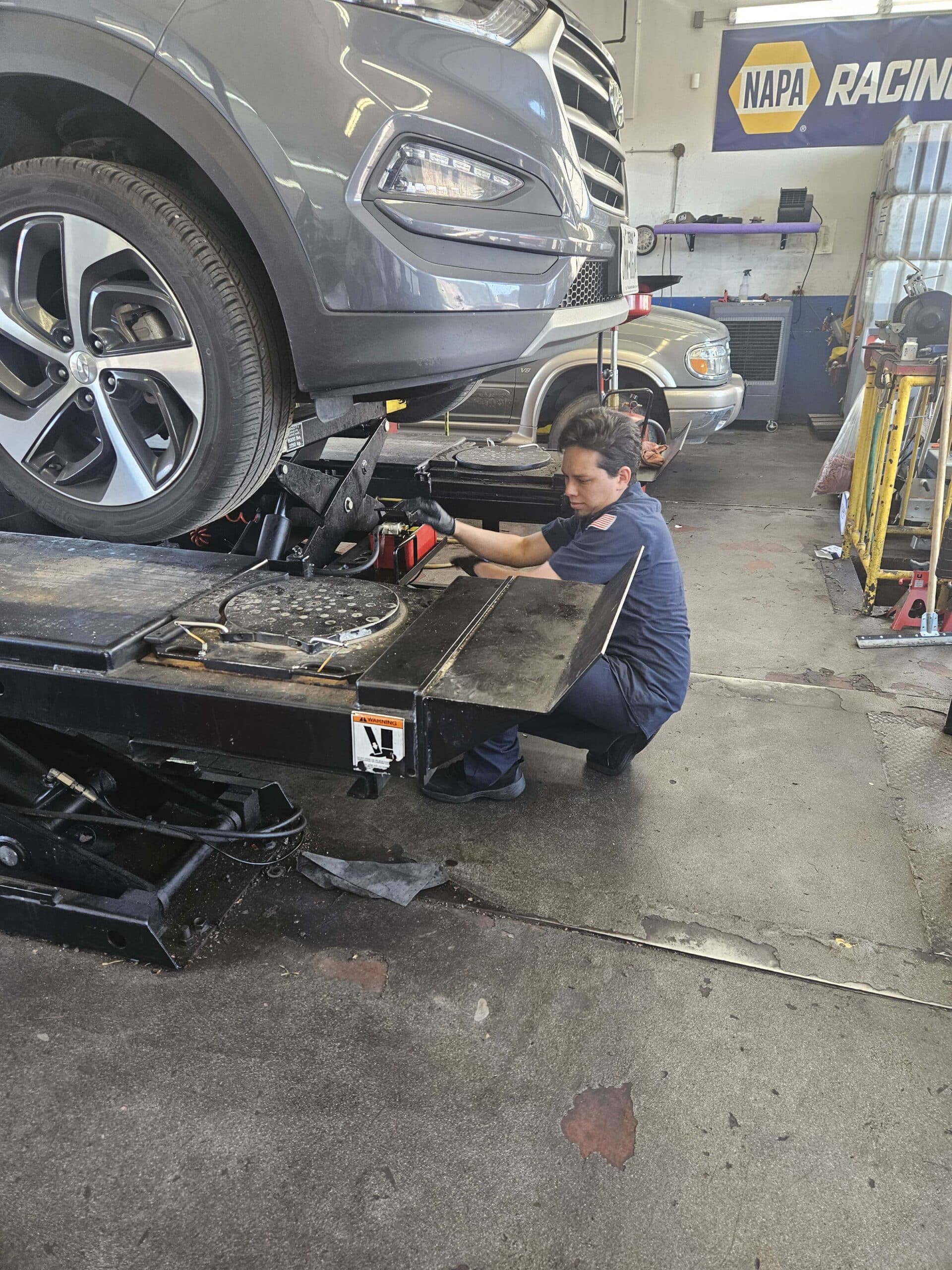 A man repairs a car in a well-organized garage, surrounded by tools and equipment.