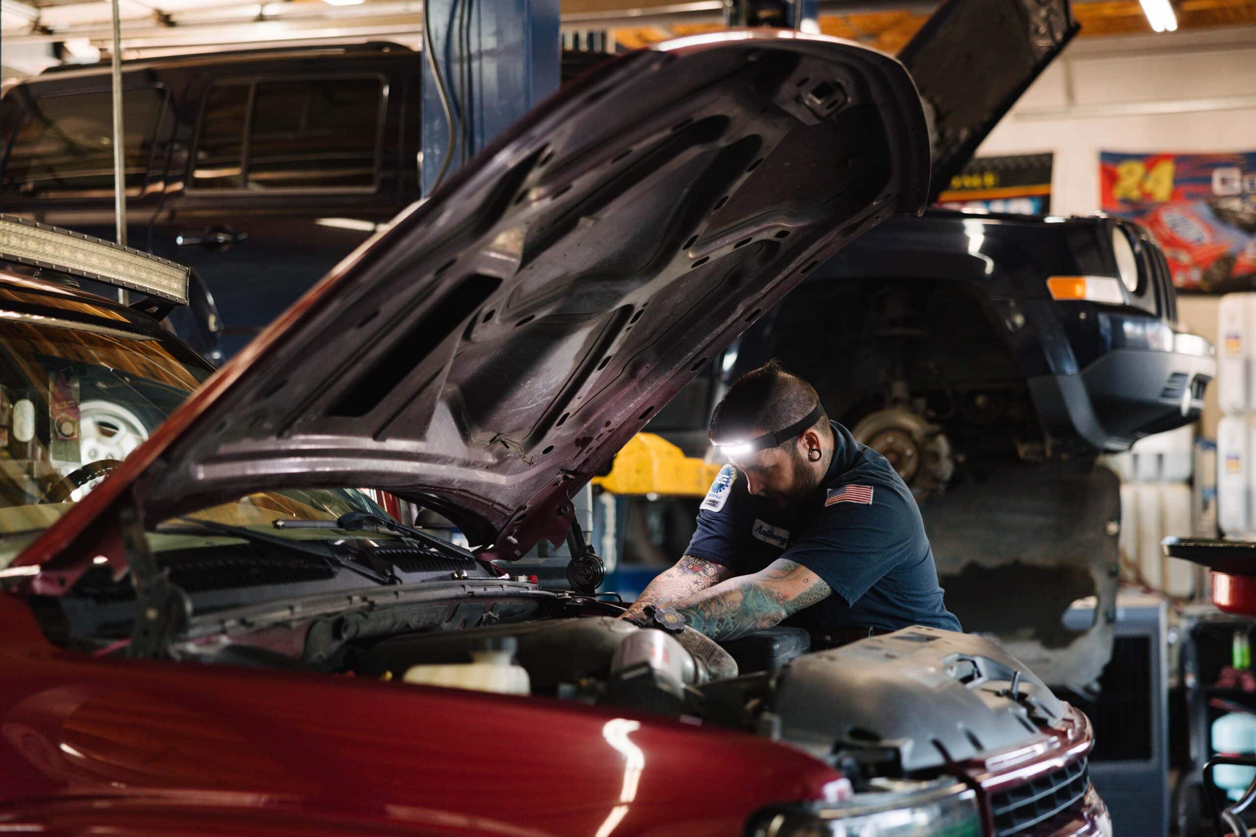 Japanese vs German cars: Which is easier to fix in Colorado Springs, CO with Express Auto Repair on Galley. Image of mechanic wearing headlight while performing repairs on a red vehicle in the shop.