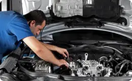 a mechanic wearing a blue shirt, working under a car hood