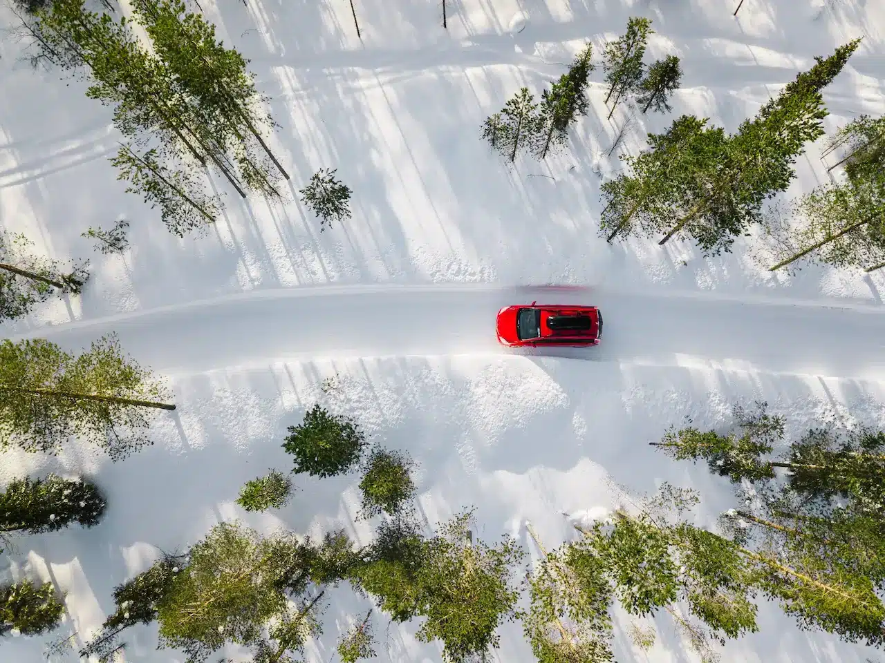 A red car navigating through a snowy landscape, showcasing winter driving conditions.