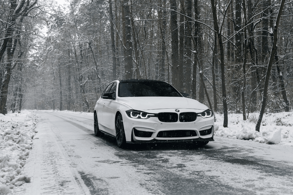 Winter Car Repair Checklist, Auto repair in Colorado Springs, CO at Express Auto Repair & Service. Image of a white BMW driving through a snowy forest road, highlighting the importance of winter vehicle maintenance and safety checks.