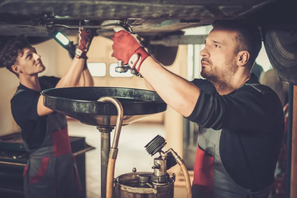 Two men inspecting the engine of a car, focused on repairs under the hood in a well-lit garage setting.