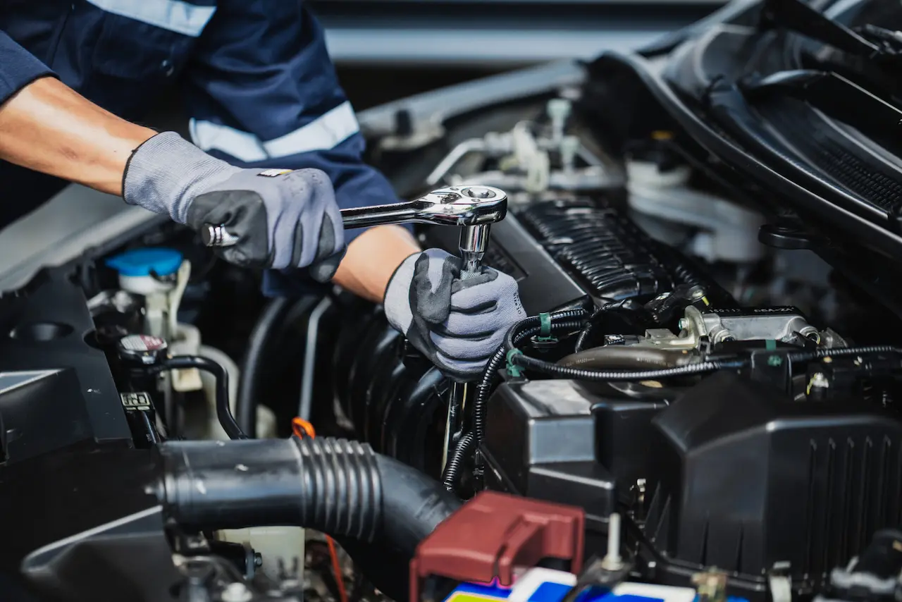 A mechanic inspects and repairs the engine of a car in a well-lit garage setting.