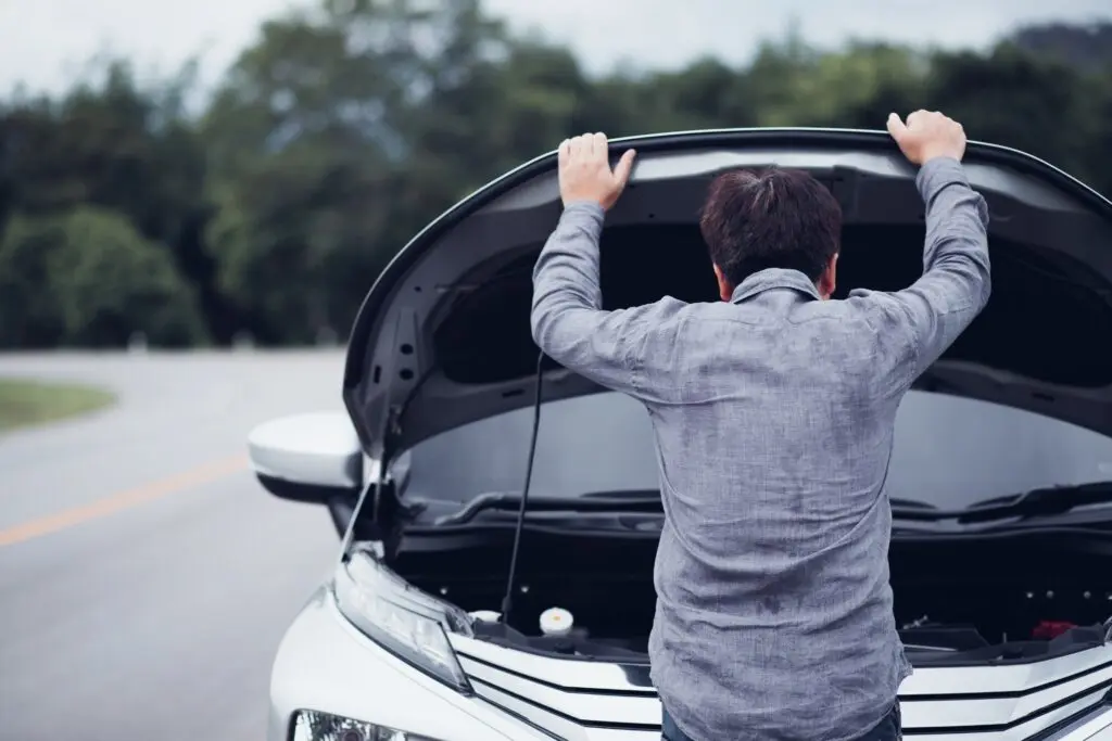 A man examines the engine compartment of a car, hood open, assessing potential mechanical problems