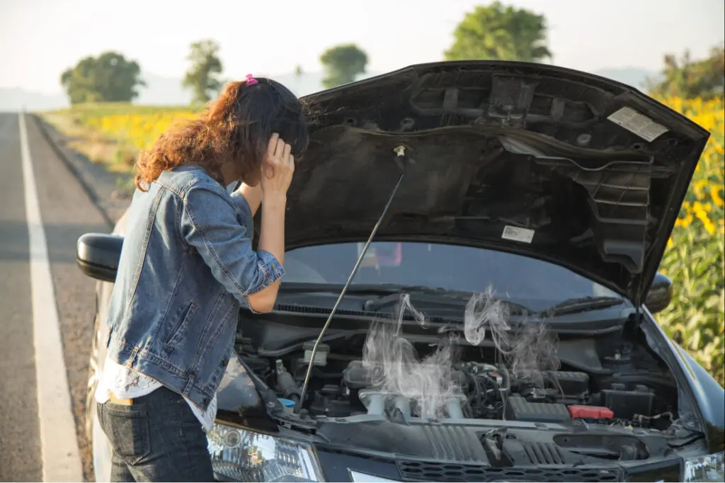 A woman stands beside her overheated car