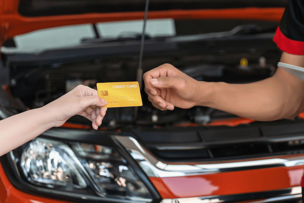 auto repair credit cards, auto repair in Colorado Springs, CO at Express Auto Repair. Image depicting a customer handing over a credit card to a mechanic in front of an open car hood.