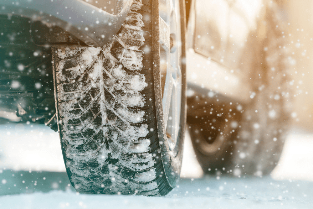 winter tire quotes, auto repair in Colorado Springs, CO at Express Auto Repair. Close-up of a car tire covered in snow, driving on a winter road with snowfall.